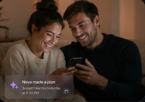 A couple sitting close together at home, smiling at a phone one of them is holding.